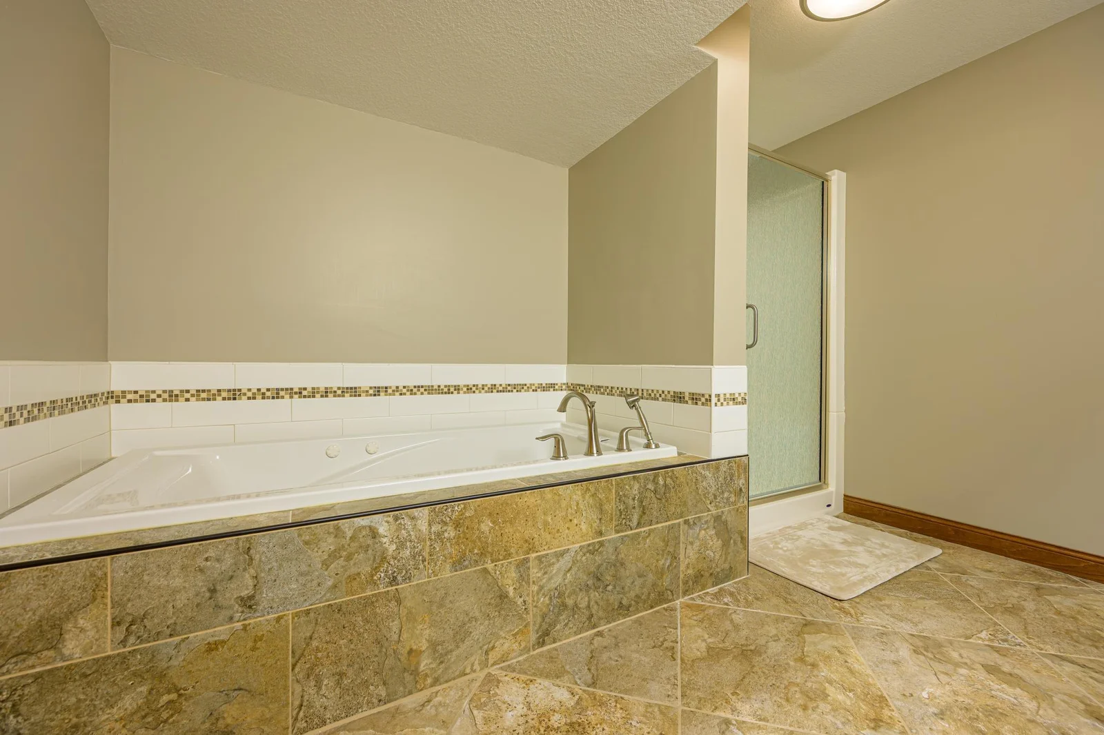 The lower level bathroom features tile flooring, a whirlpool tub with a tile surround, and a separate walk-in shower.