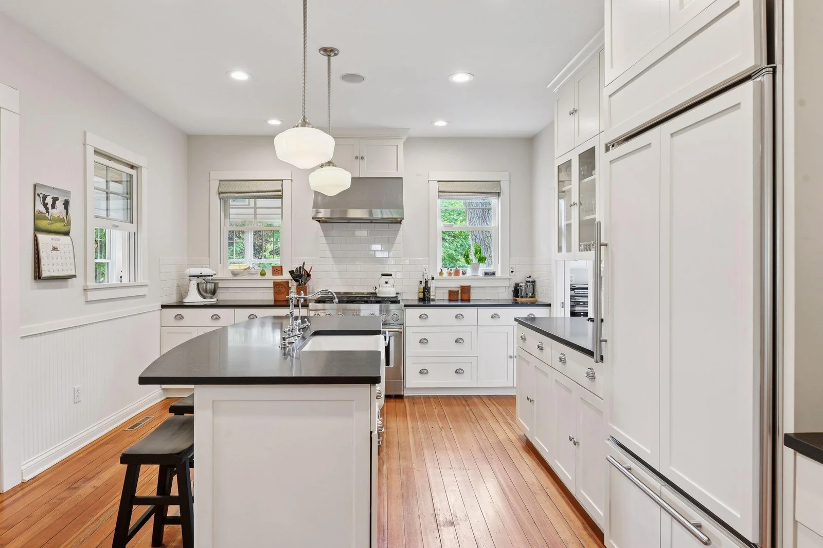 Beautifully updated kitchen featuring a gas range with custom hood, farmhouse sink, and warm wood floors
