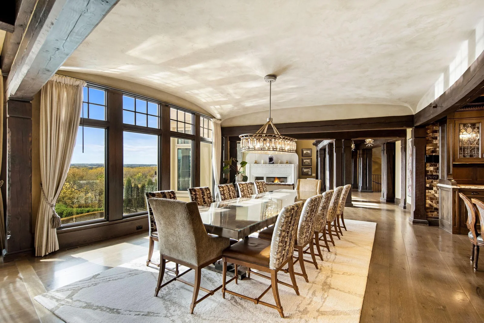 The dining room is a grand spectacle, featuring massive windows that showcase panoramic views of the breathtaking landscape beyond. Sunlight pours in, illuminating the space and enhancing the warm tones.