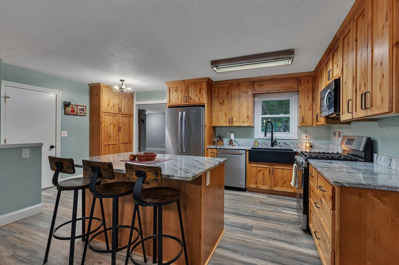 Renovated kitchen features updated cabinetry, stone countertops, island, and stainless steel appliances.