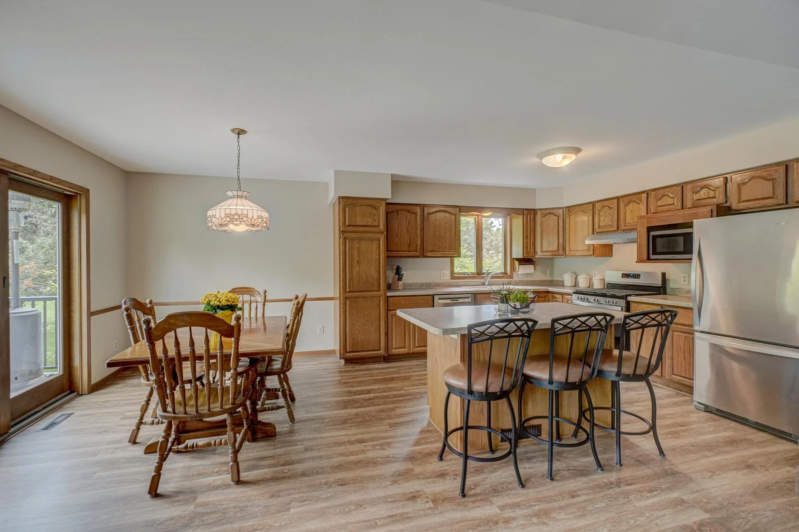 The kitchen features a center island, ample cabinets, and generous counter space, flowing seamlessly into the dining area and out to a large composite walkout deck—perfect for entertaining or relaxing with a view of the backyard.