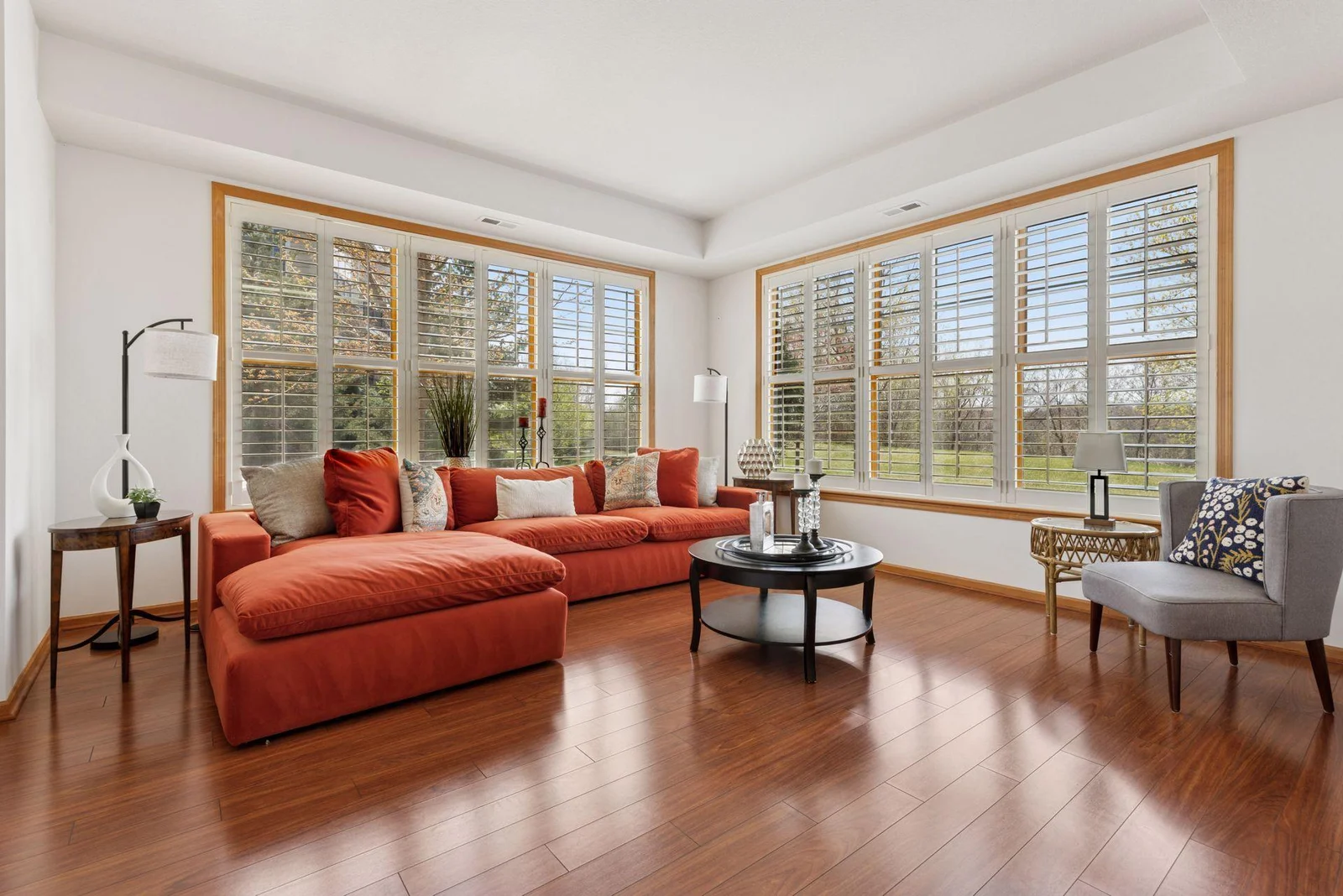 Expansive views from oversized windows, high tray ceilings, luxury wood plank flooring, and elegant white shutters.
