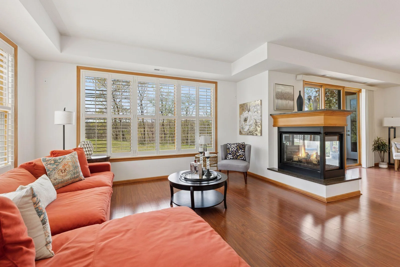 High tray ceilings, 3-sided gas fireplace, luxury wood plank flooring, and elegant white shutters overlooking the path to the lake.