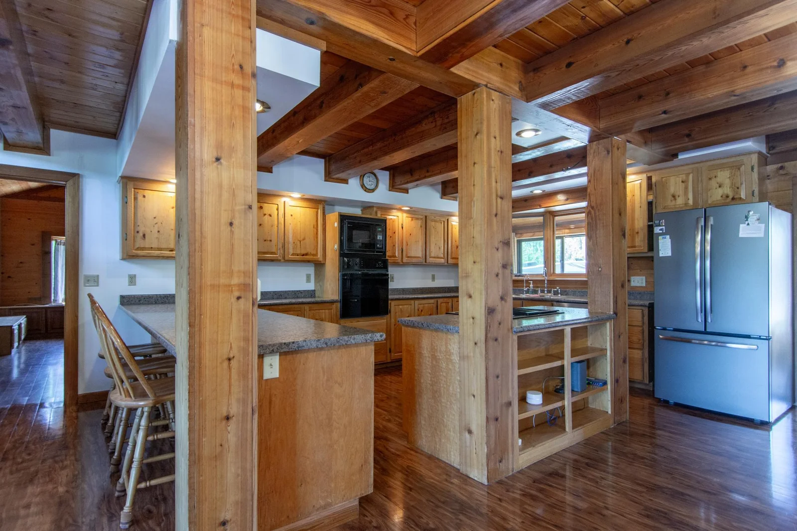 The kitchen has a vinyl floor, knotty pine cabinets, oak trim, a stainless steel fridge and dishwasher, and a west-facing window.