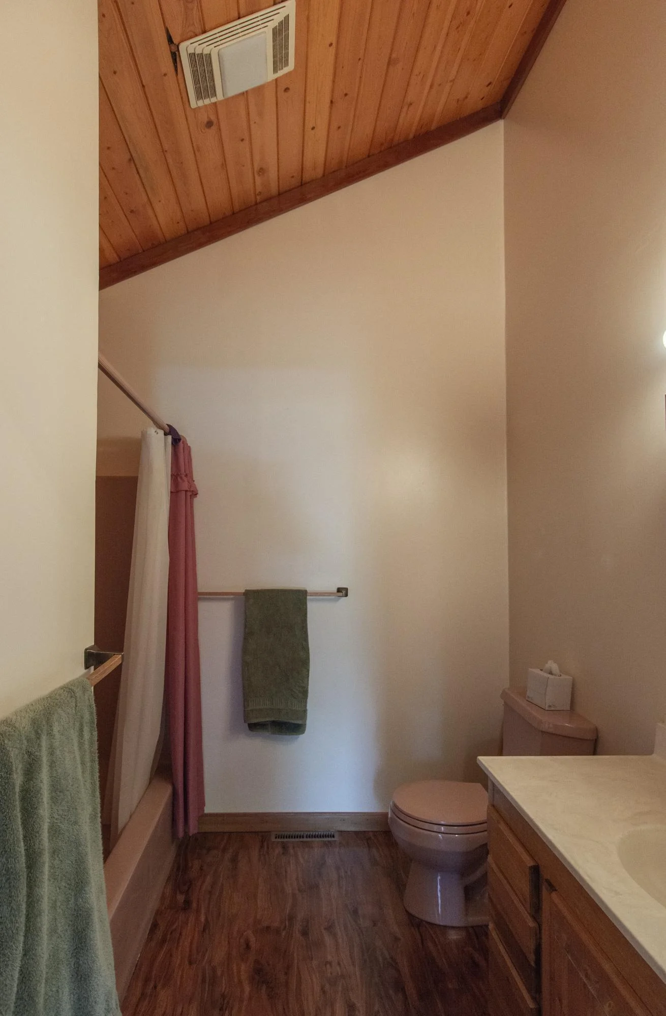 The full primary bathroom has a vinyl floor and a vaulted ceiling.