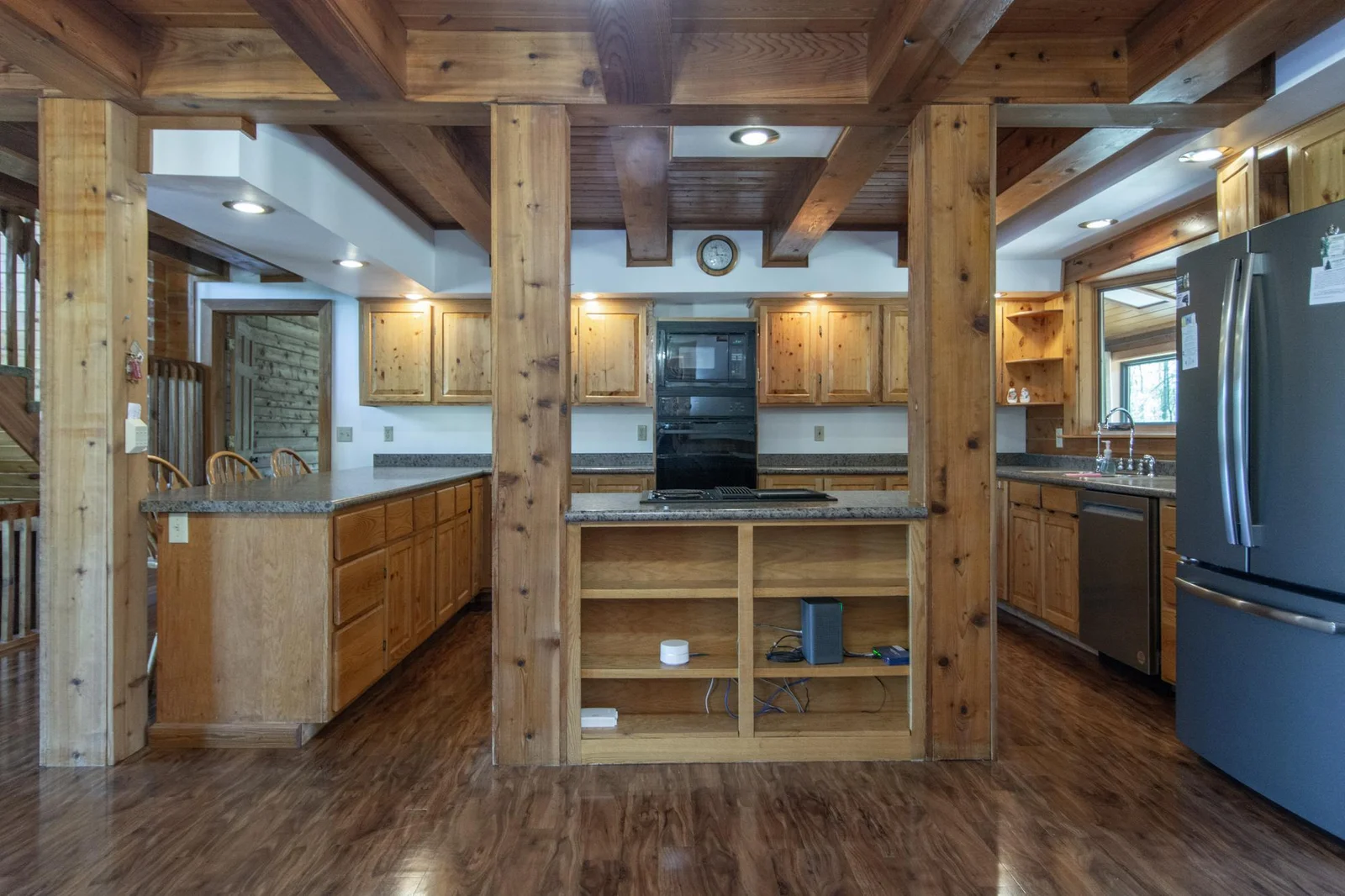 The kitchen has a vinyl floor, knotty pine cabinets, oak trim, a stainless steel fridge and dishwasher, and a west-facing window.