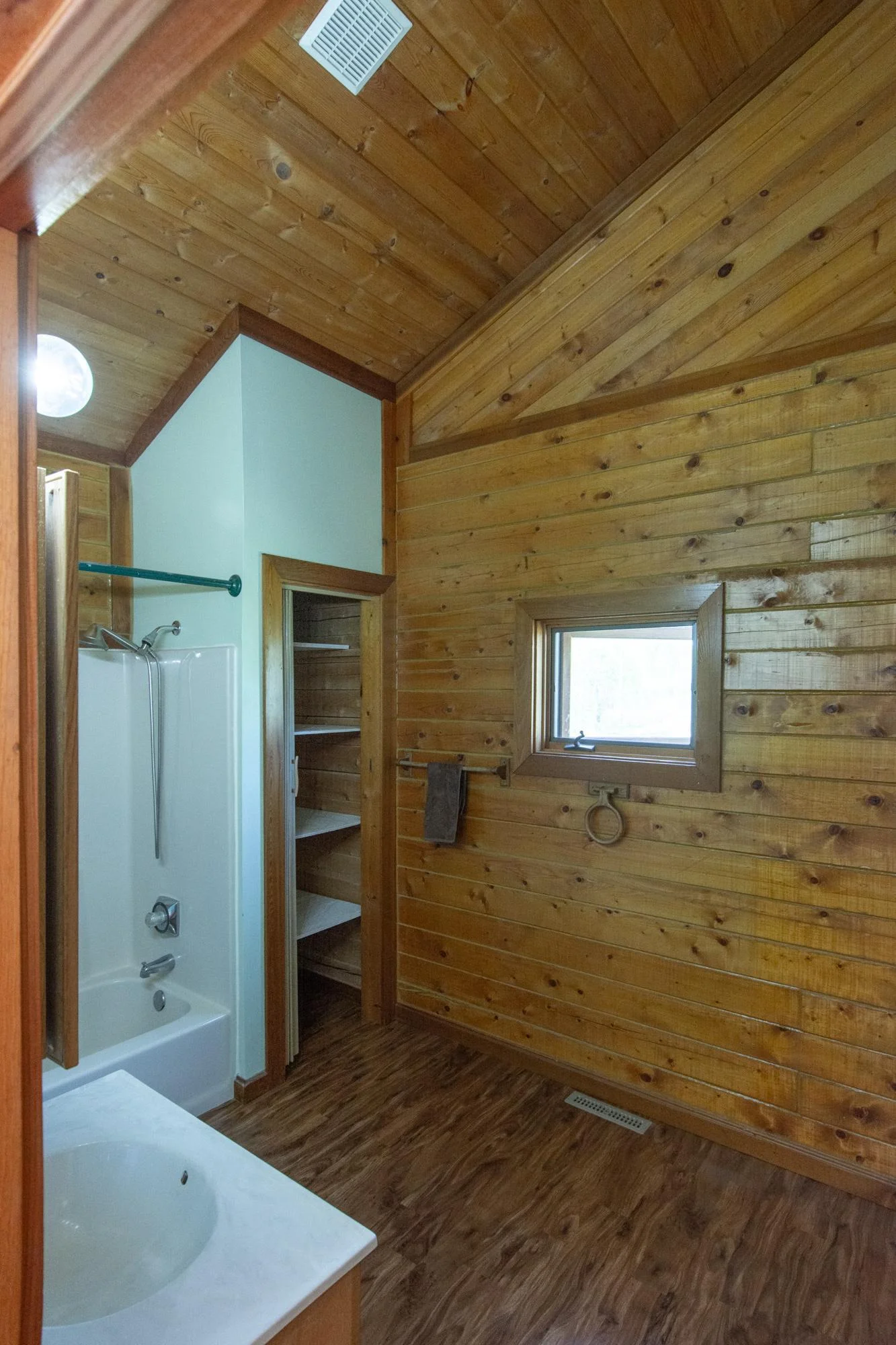 Main floor full bathroom has vinyl floor, a vaulted ceiling, a north-facing window, and a 2x3 ft. closet.