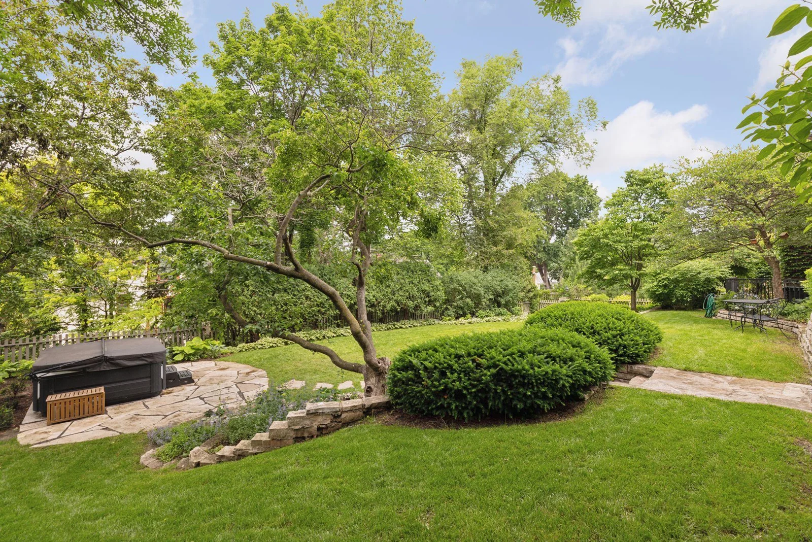 Lower level lawn with stone patio and hot tub area. Mature hedges provide privacy and natural beauty.