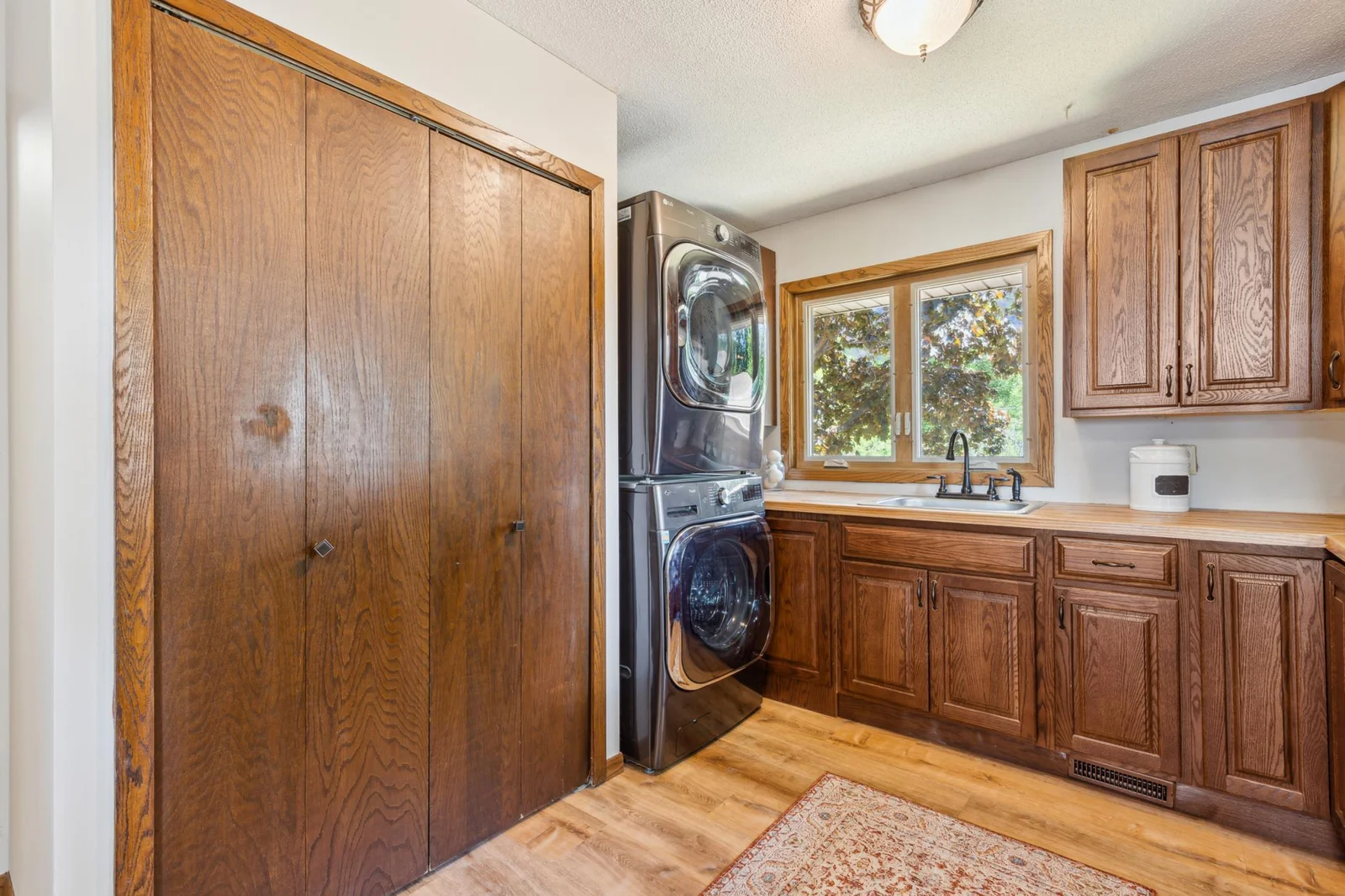 Spacious laundry area featuring modern stacked washer and dryer, ample cabinetry, a utility sink, and large window for natural light.