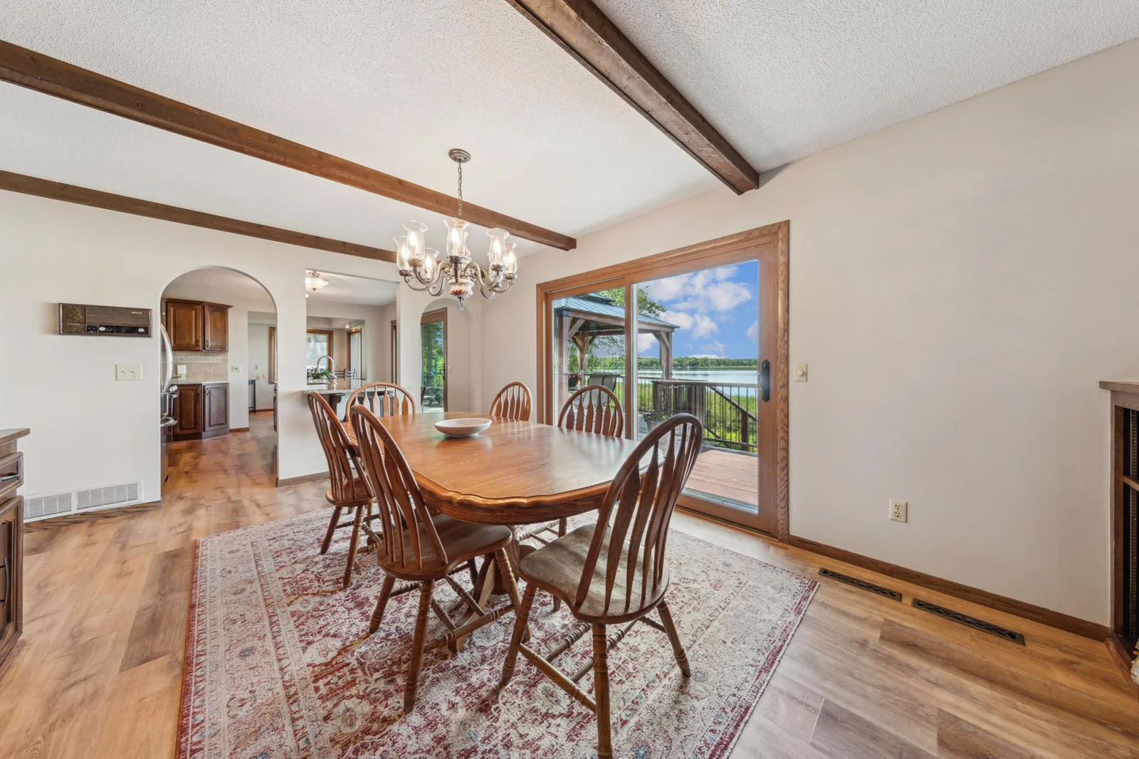Formal dining room with wood beam ceiling, chandelier lighting, and sliding glass doors to the lakeside deck—perfect for dinner with a view.