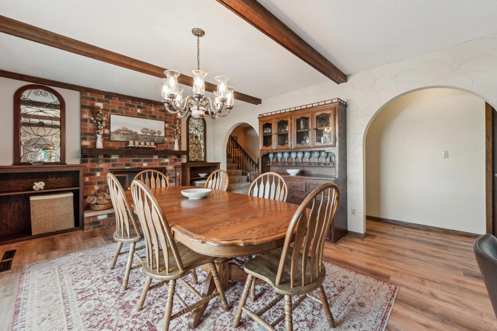 Brick fireplace adds warmth and character to this elegant dining room featuring wood-beamed ceilings and built-in shelving.