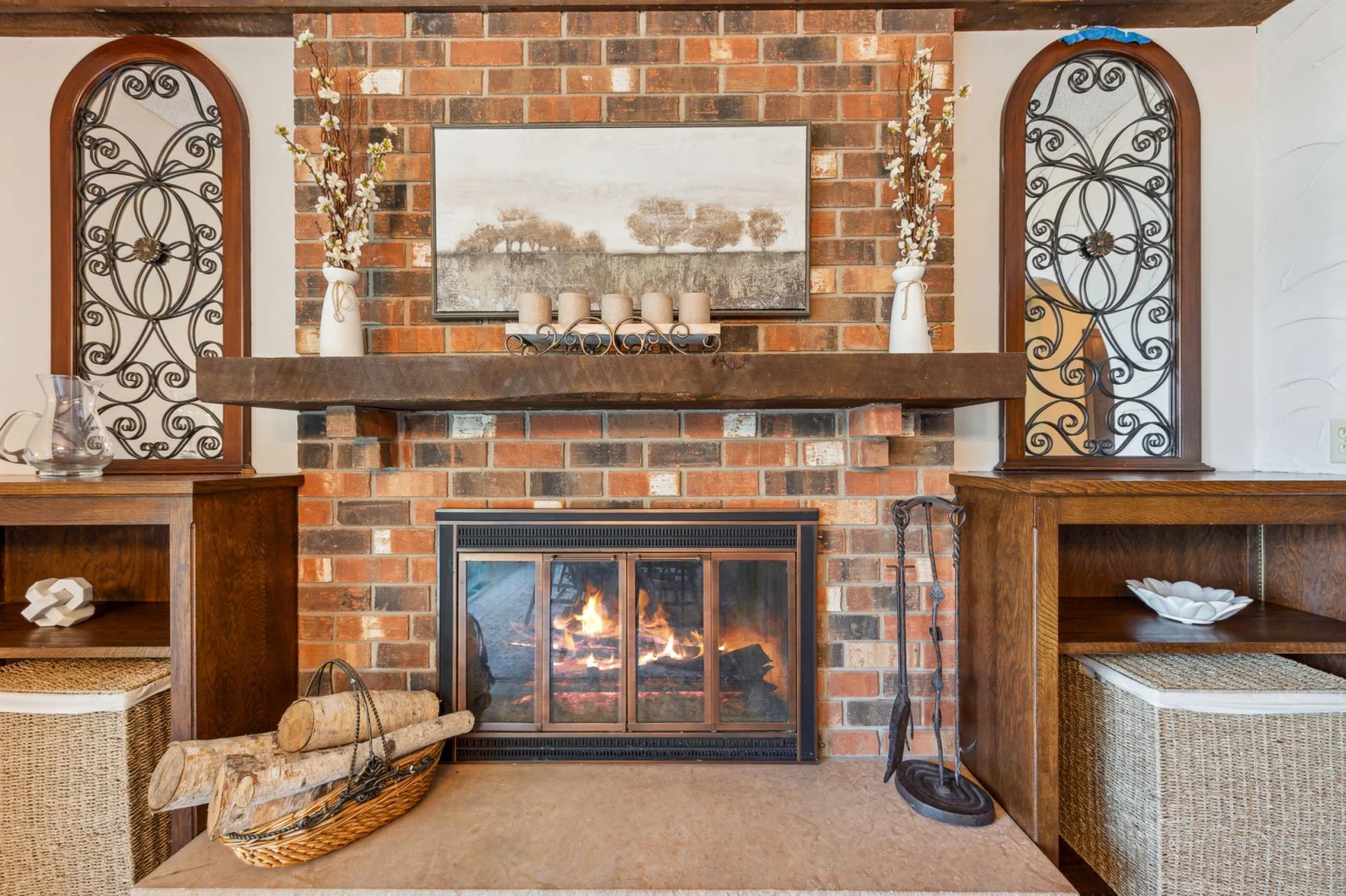 Beautiful brick surround fireplace with a rustic wood mantel, built-in shelving, and charming decorative ironwork—perfect for cozy evenings.