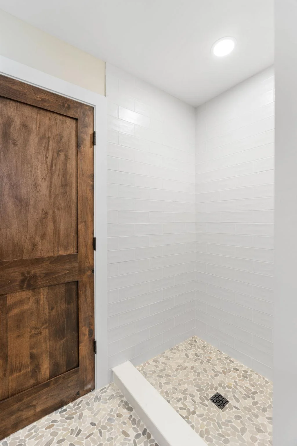 Custom shower features subway tile surround and frameless glass enclosure + natural pebble flooring throughout