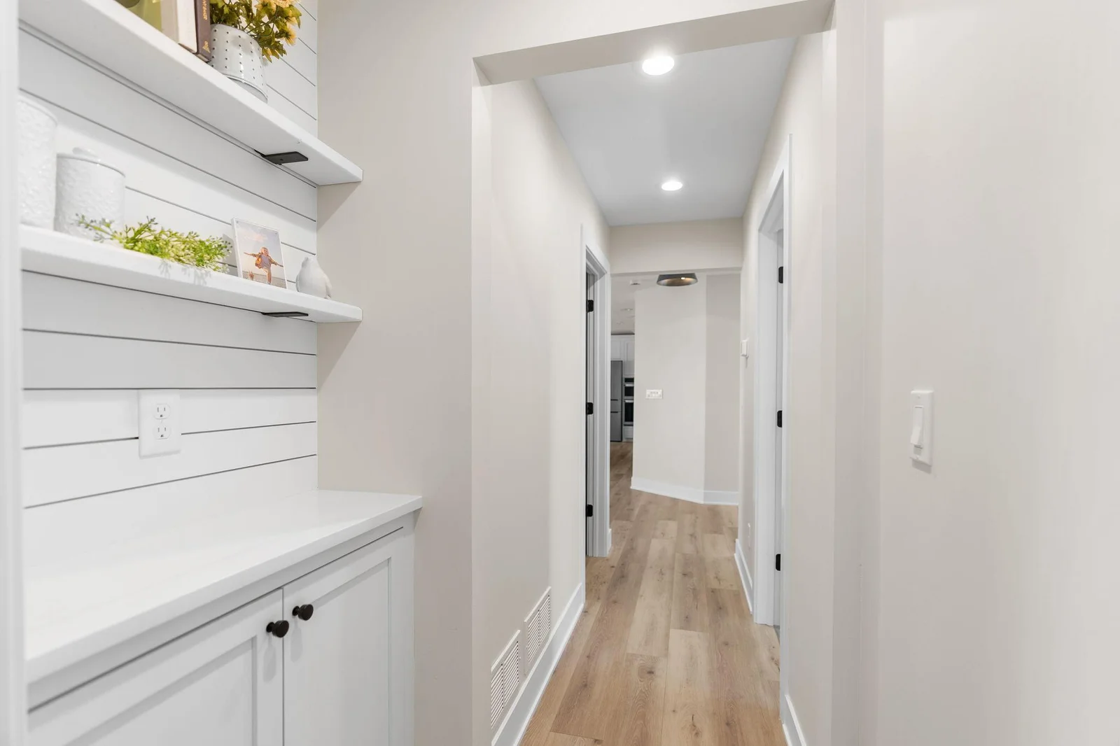 Hallway features display niche that offers a built-in enameled cabinet w/ quartz top, enameled wood paneled accent wall and floating shelves