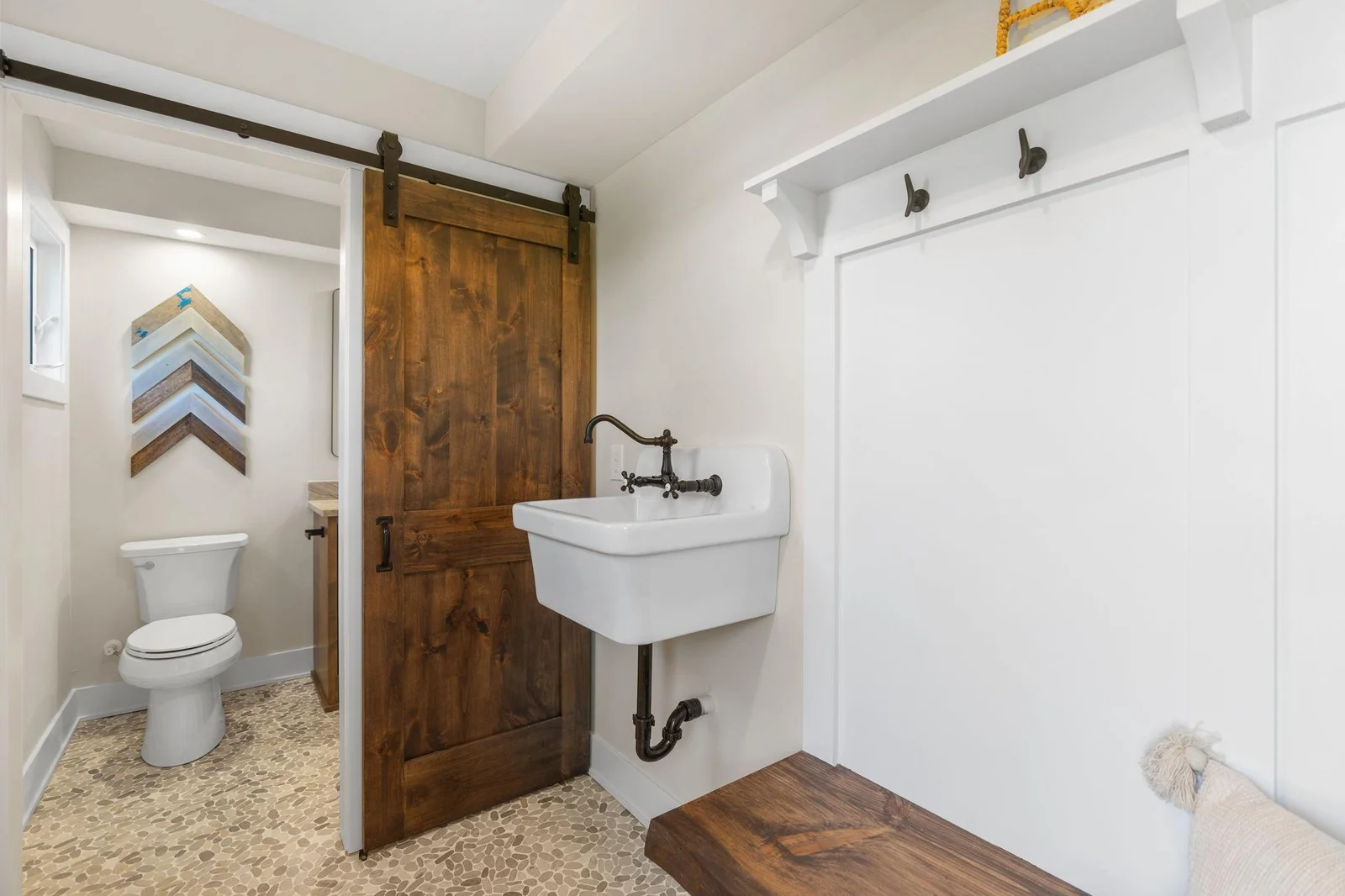 Lakeside Mudroom features barn door access to the 3/4 bathroom, natural pebble flooring and suspended porcelain utility sink