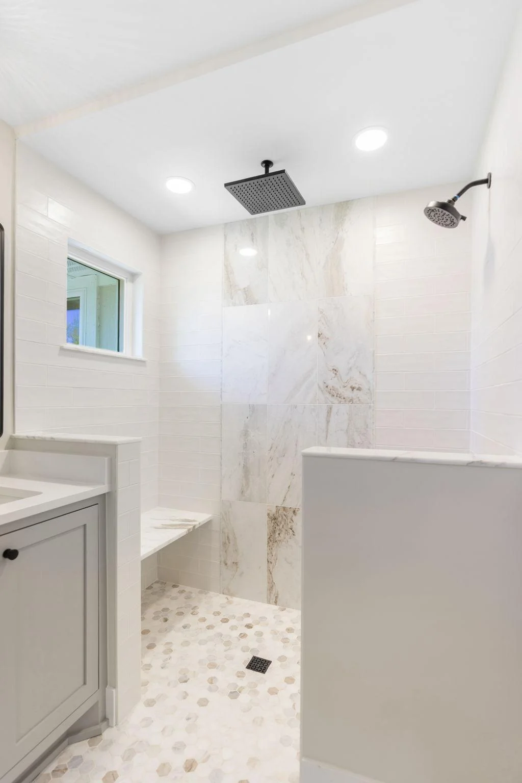 Curbless walk-in shower features tile surround, stone bench, additional rain shower head and glass enclosure