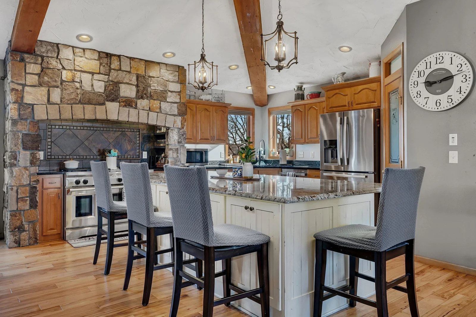 Large granite center island is the centerpiece of this kitchen and is a beautiful contrast to the stone range and hood feature.