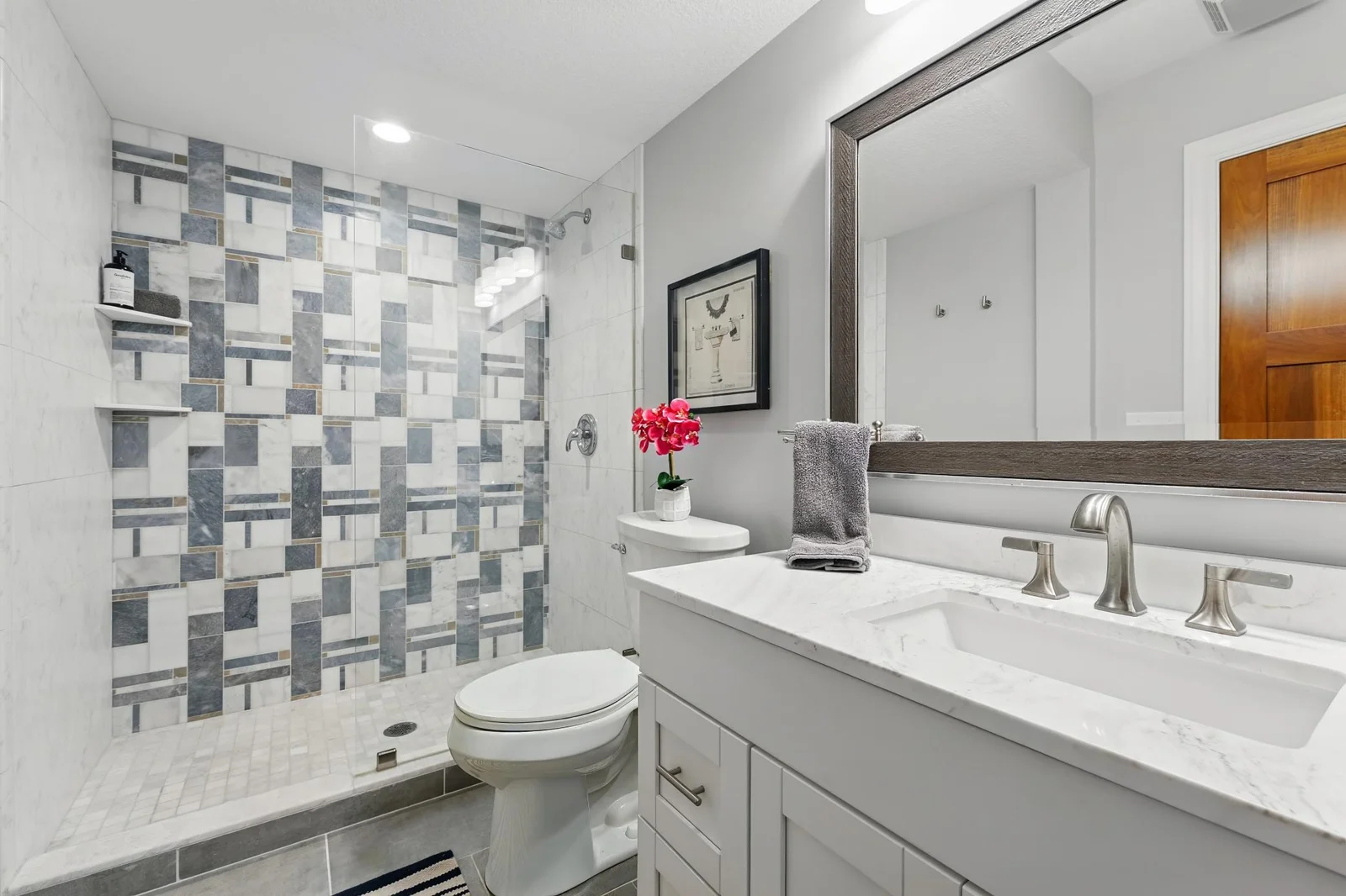 The lower level bath features tile floors, tile base trim and a tile shower surround. It also features an upgraded vanity cabinet with quartz counters and an undermount sink.