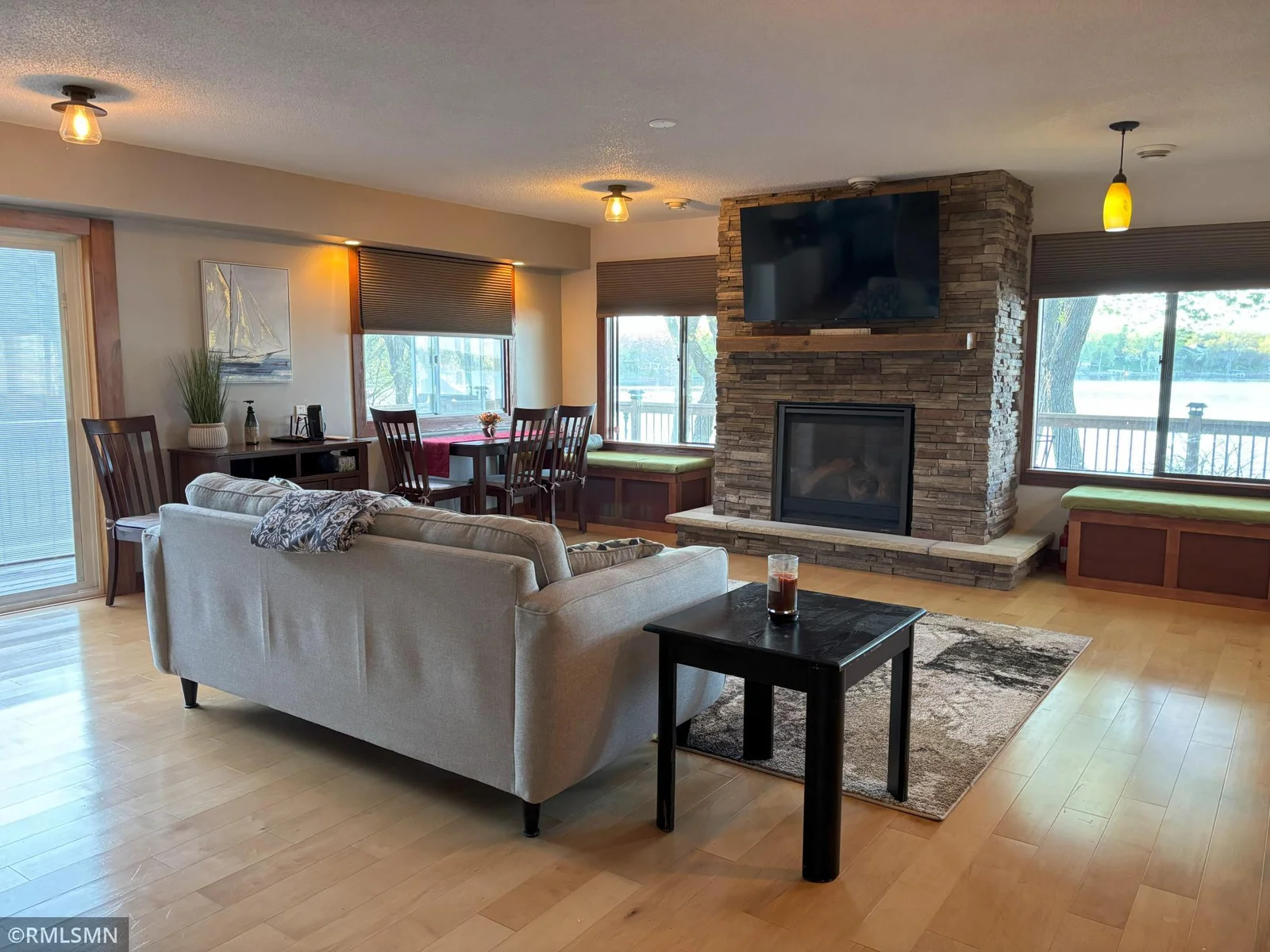 Open living room with seating benches, walled with windows, gas fireplace, with mounted tv and hardwood floors