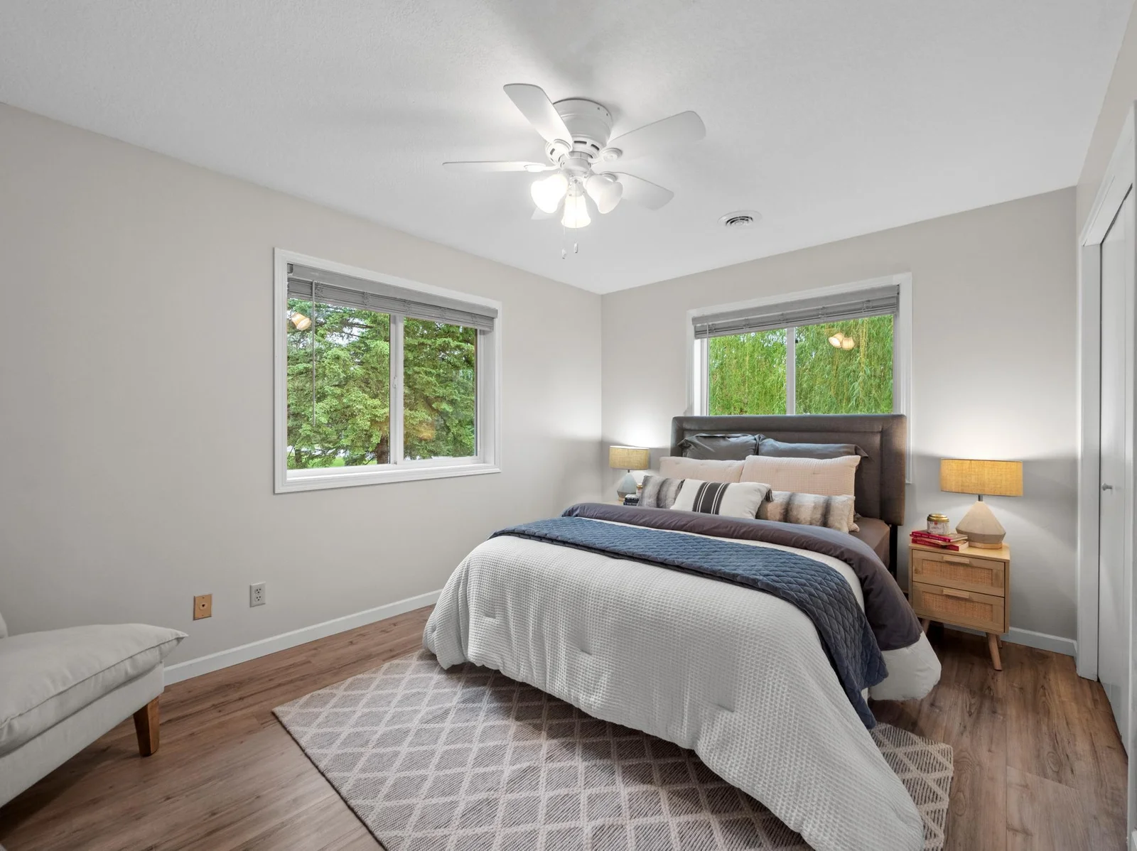 The primary bedroom oasis features neutral colors, abundant natural light streaming through the dual windows, and a ceiling fan for added comfort year-round.