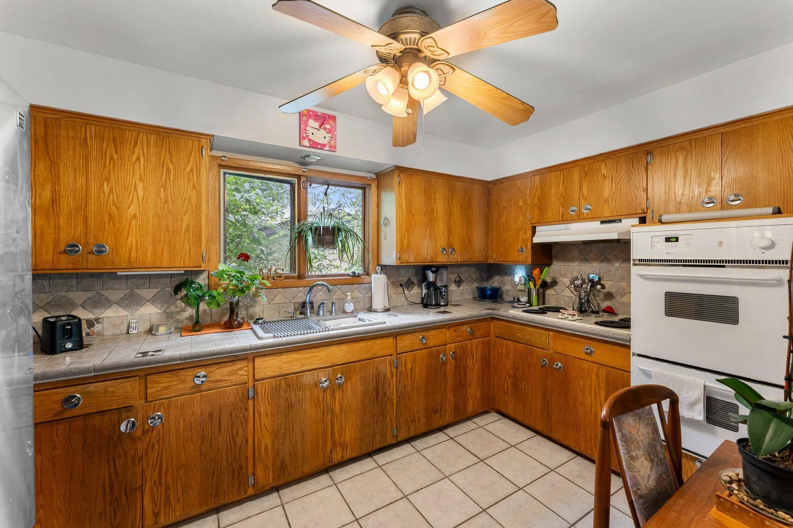 The bright kitchen is surrounded by windows and features tile flooring, tiled countertops and backsplash, and ample cabinetry—offering plenty of storage.