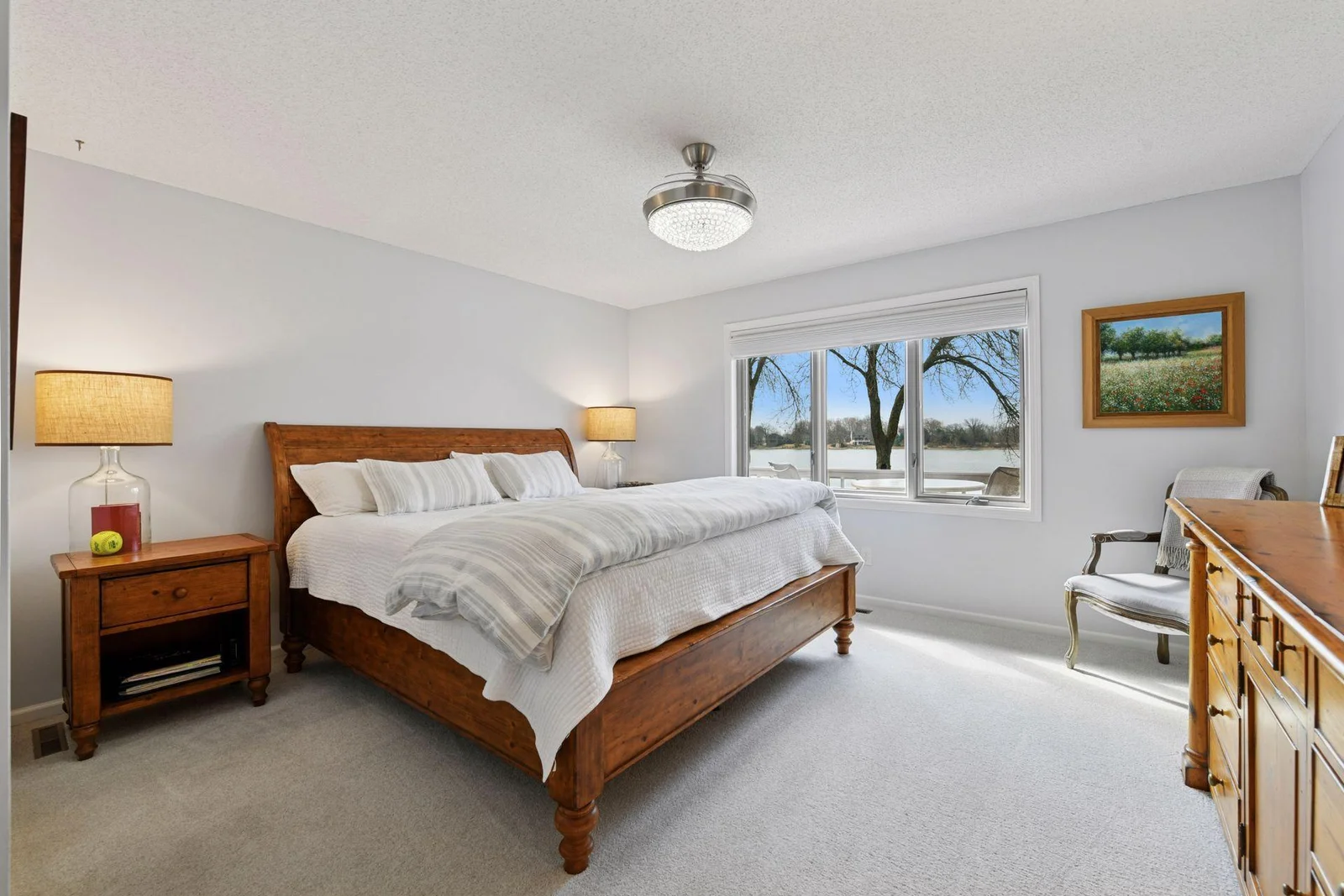 Welcome to the lakeside-facing primary suite—open your windows to enjoy the soothing sounds of the water and the refreshing summer breeze in this generously sized bedroom.