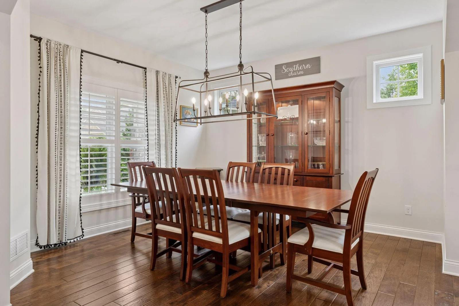 The formal dining room showcases elegant wood floors and a stylish light fixture that adds a touch of sophistication. A large window brings in abundant natural light, creating a warm and inviting atmosphere.