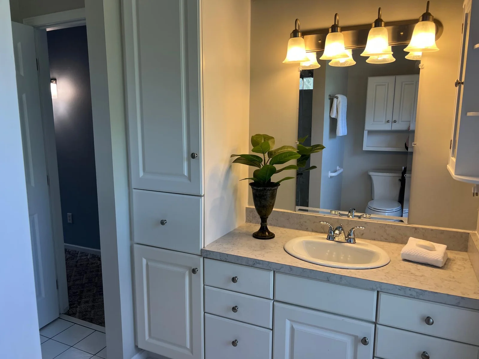 THE PRIMARY BATH VANITY, WITH A VIEW TO THE HALL THAT LEADS TO THE BEDROOM.
