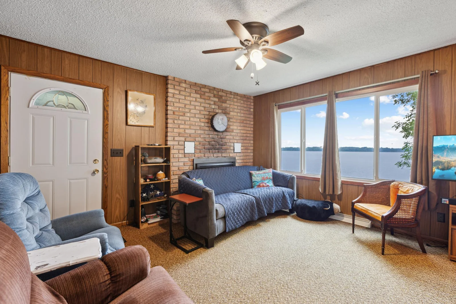 The oversized windows offer panoramic views looking out over Lake John. Perfect for taking in the evening sunset across the water. Hidden behind the couch is a gas insert fireplace. The home also has a forced air furnace with AC but is seasonal.