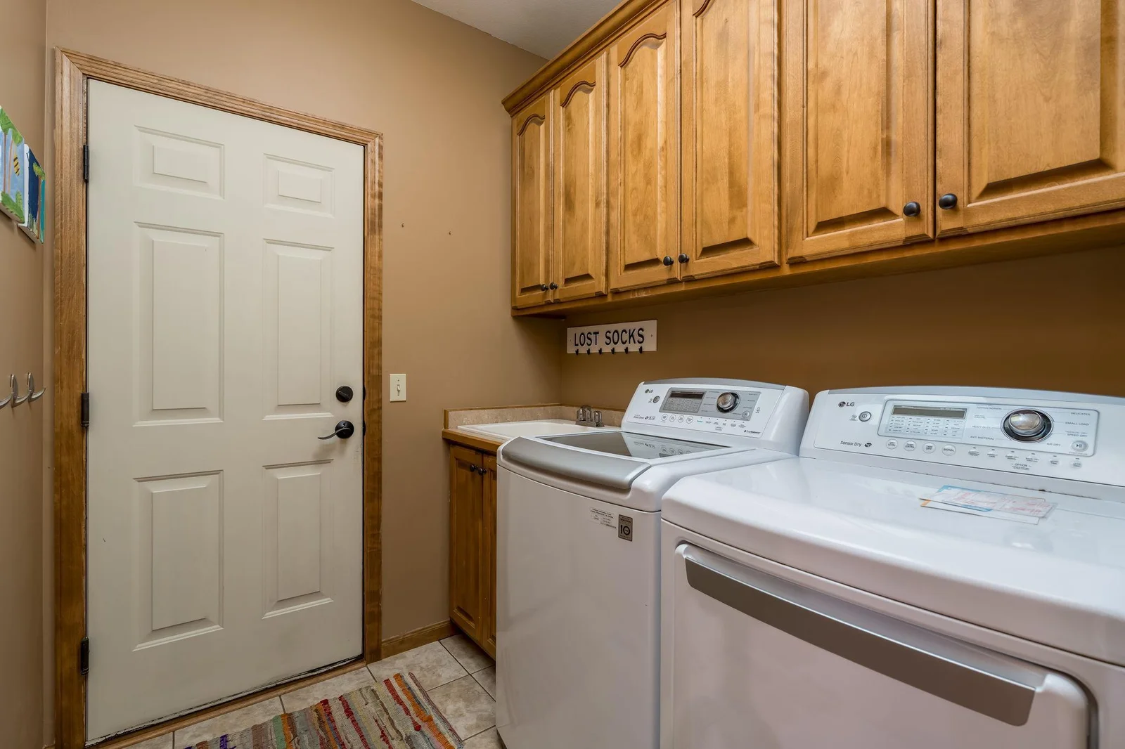 Main floor laundry / mudroom with tiled floors, sink and upper cabinets.