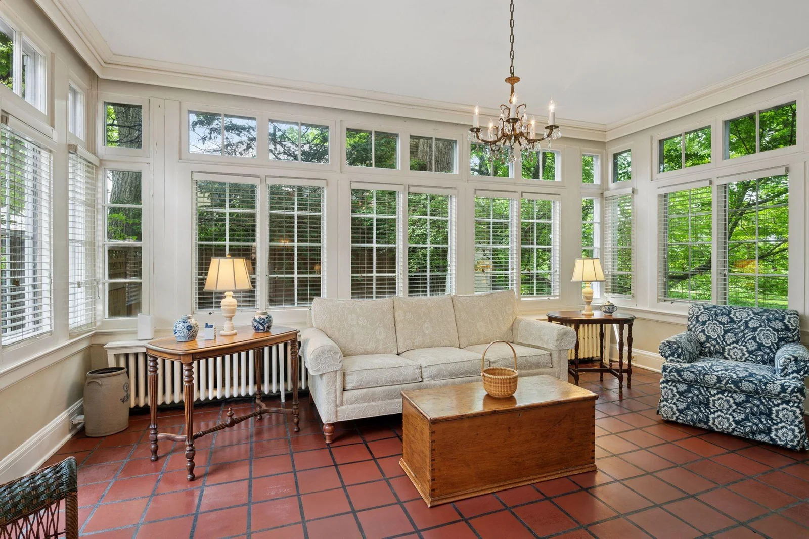 The sunroom with walls of windows and original clay tile flooring has access to the back patio.