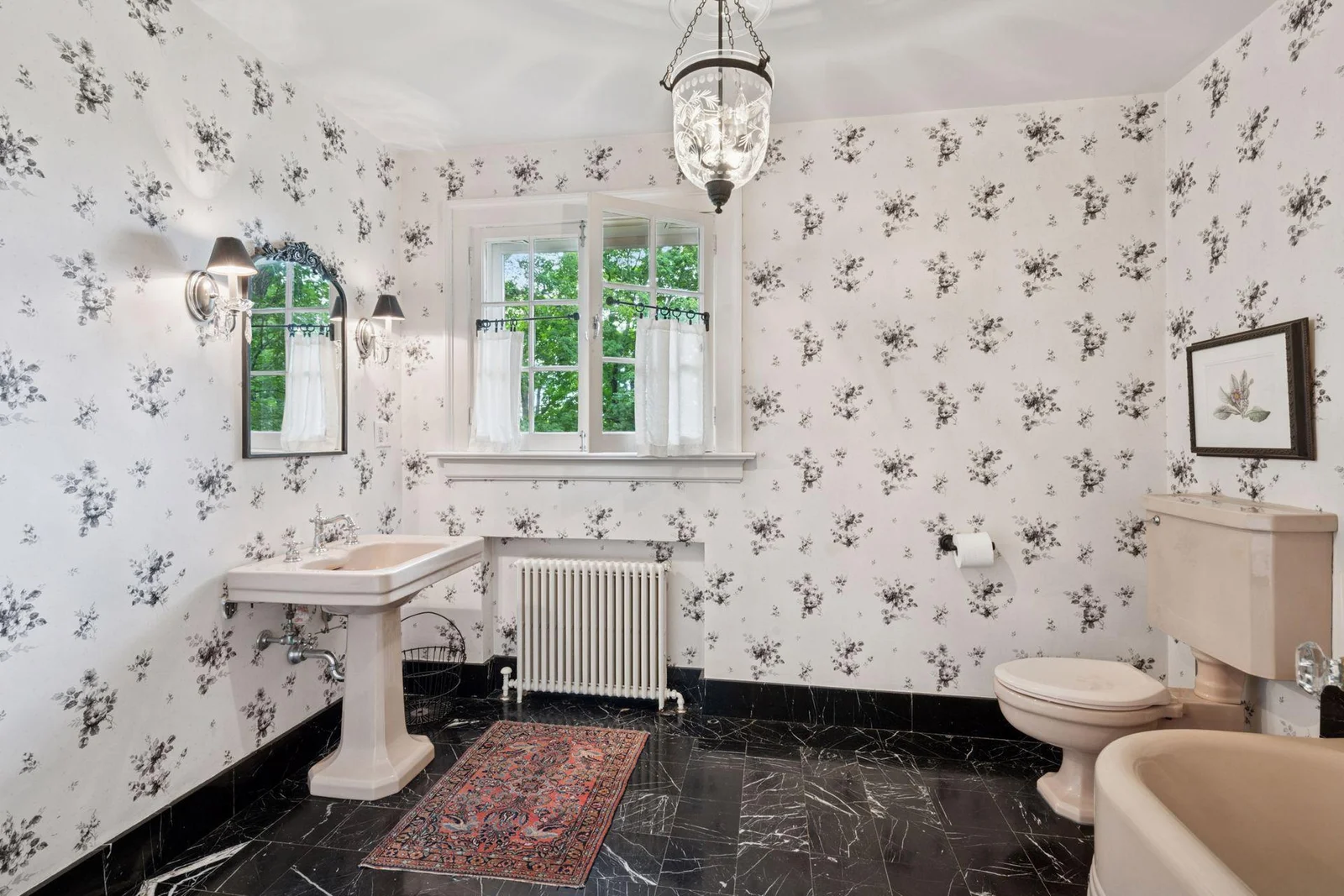 This hall bath is oversized, yet charming with black and white floral wallpaper and marble floors.