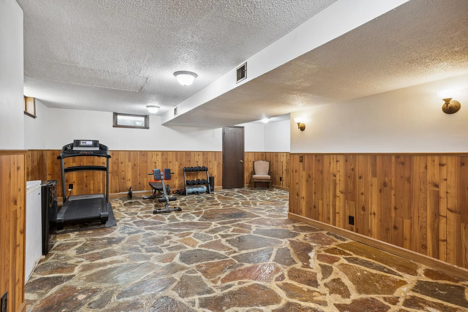 Basement workout space can be used for a playroom or family room. Wall sconce lights area could be a great space for a basement bar area.