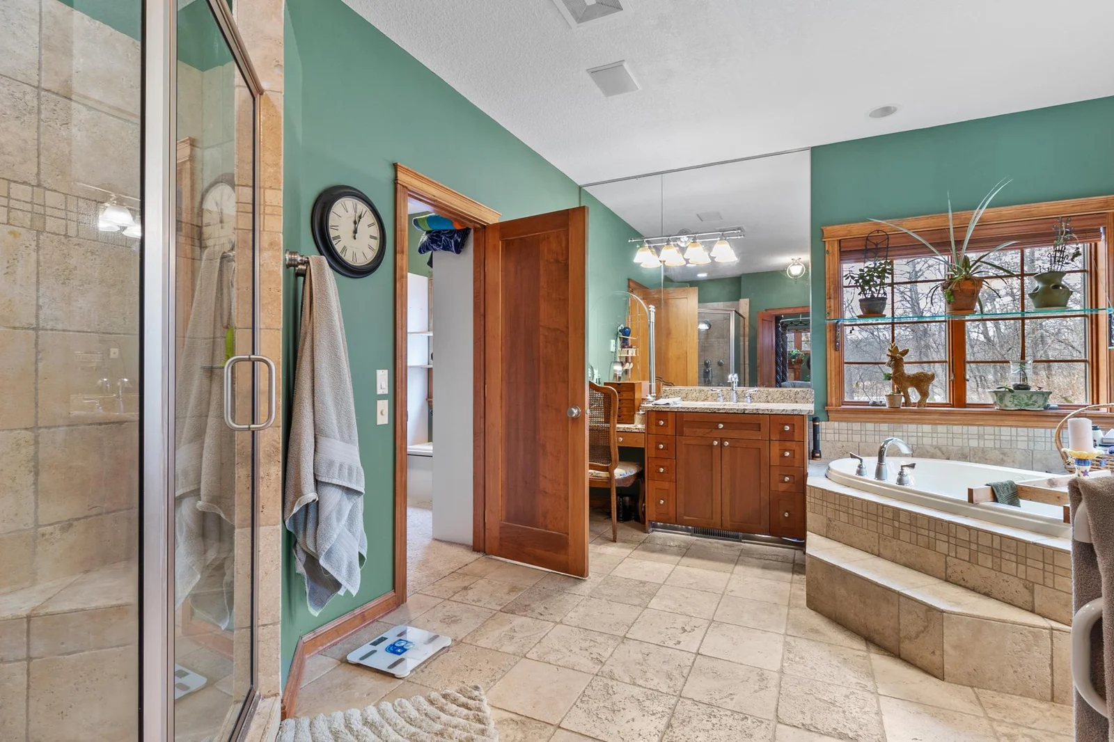 Primary bath with custom tile flooring and custom tile shower. Large tub with jets. Two separate sink areas and dressing table. Entry to second primary walk-in closet shown.