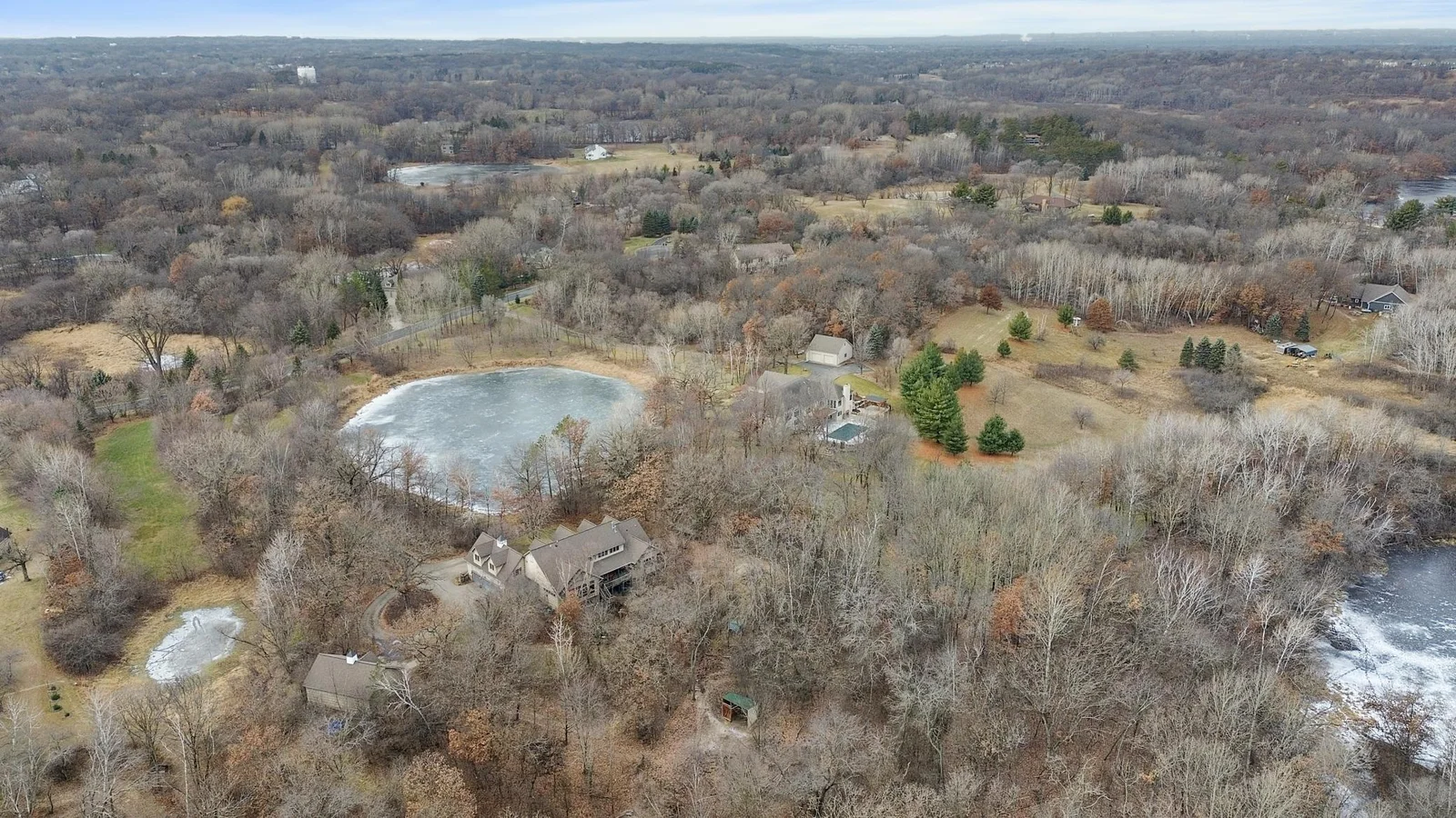 Wider view looking west showing that property extends west beyond the large pond to Coffee Trail. Shows the mixture of lawns, woods, mature trees, and landscaping with horse paddock and run in shelter shown in foreground.