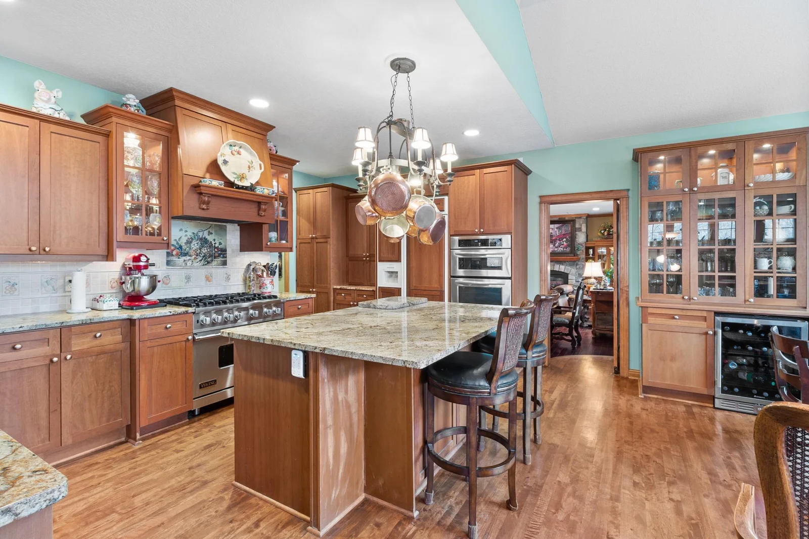 Kitchen showing vent-a-hood over Viking stove. View toward butler door to formal dining and wine refrigerator featuring lighted glass storage and display cabinet.