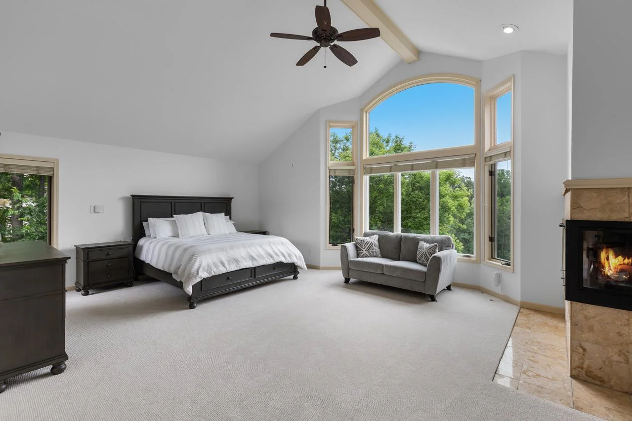 The expansive primary bedroom is a true sanctuary, featuring soaring vaulted ceilings, a cozy fireplace, and dramatic floor-to-ceiling windows that flood the space with natural light.