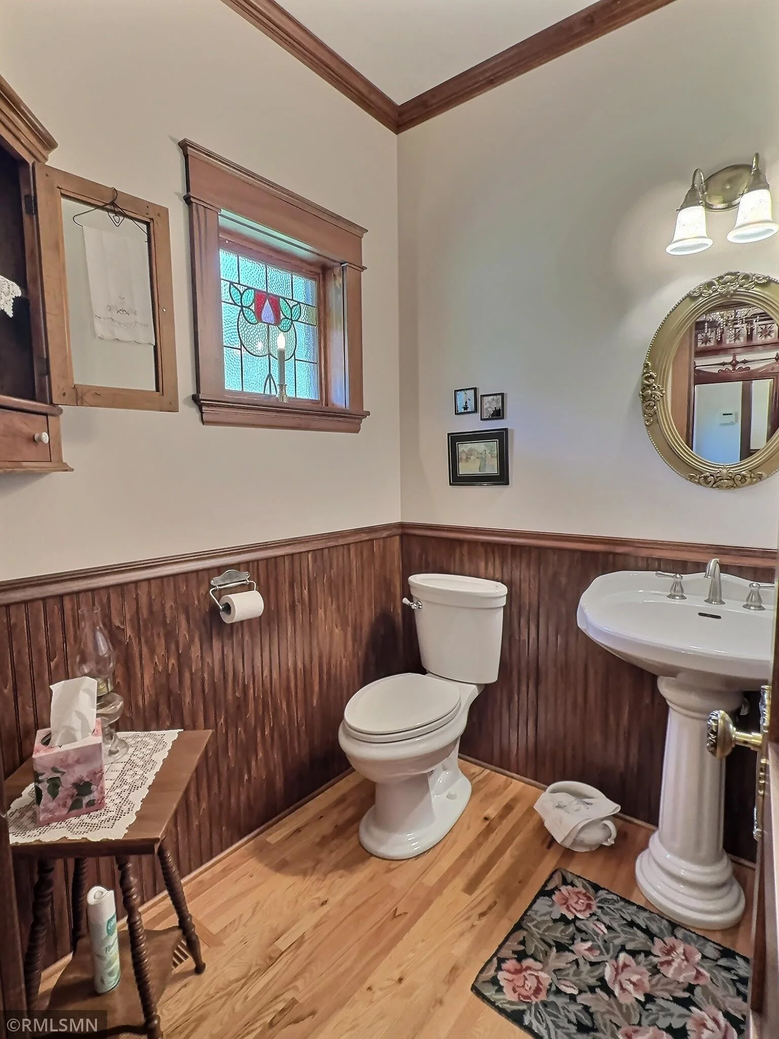 The main level half bathroom blends vintage elegance with everyday functionality with arm wood wainscoting and a classic pedestal sink.