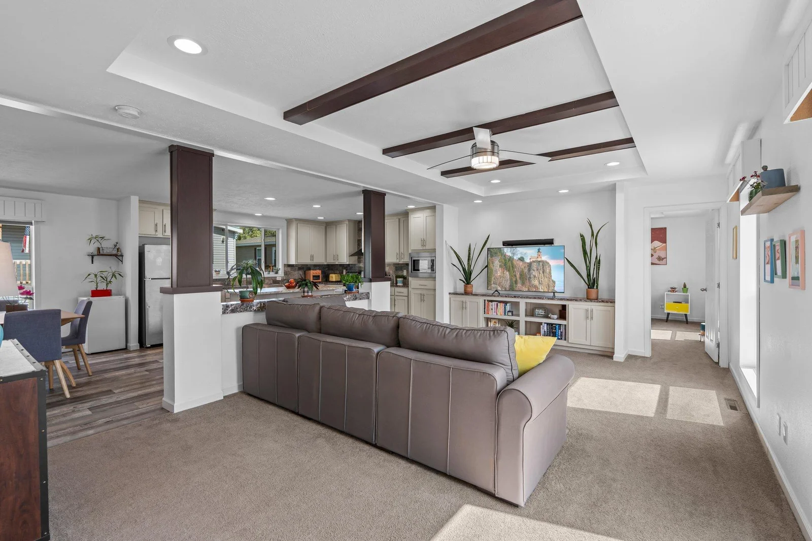 The spacious living room features plush carpeting, a ceiling fan for year-round comfort, and striking wood ceiling beams that add warmth and architectural charm.