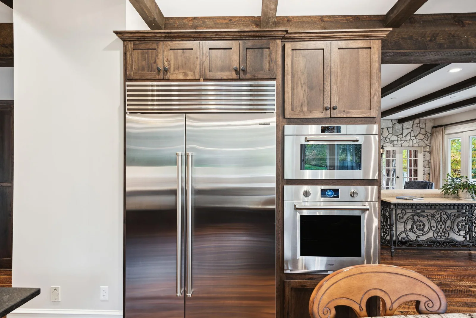 Top-of-the-line Sub-Zero refrigerator and Wolf double ovens complement the custom cabinetry and exposed beams, offering both function and elegance in this chef-inspired luxury kitchen.
