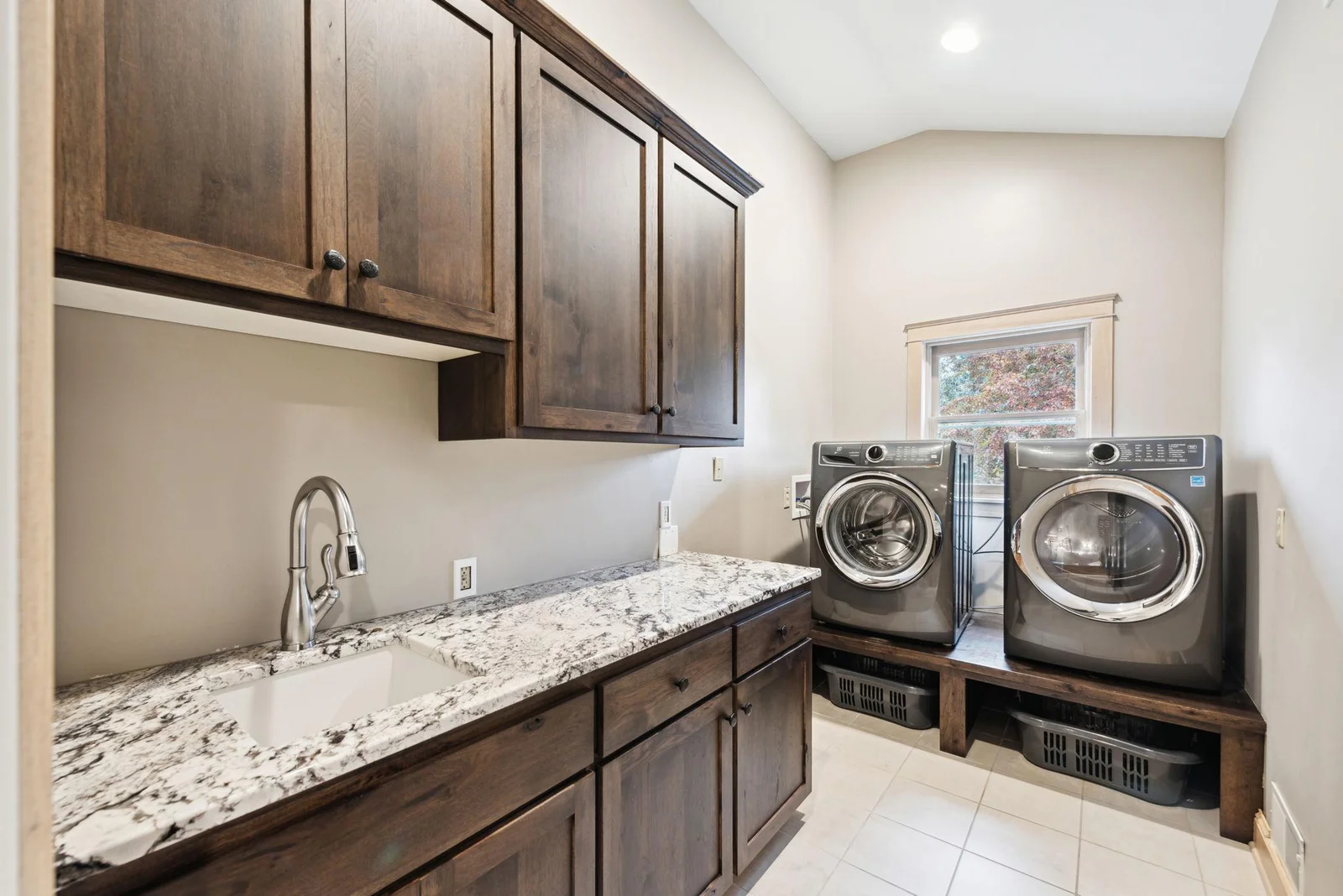 This upper-level laundry room offers convenience and style with granite countertops, custom cabinetry, and elevated washer/dryer with built-in storage. Centrally located near four of the bedrooms.