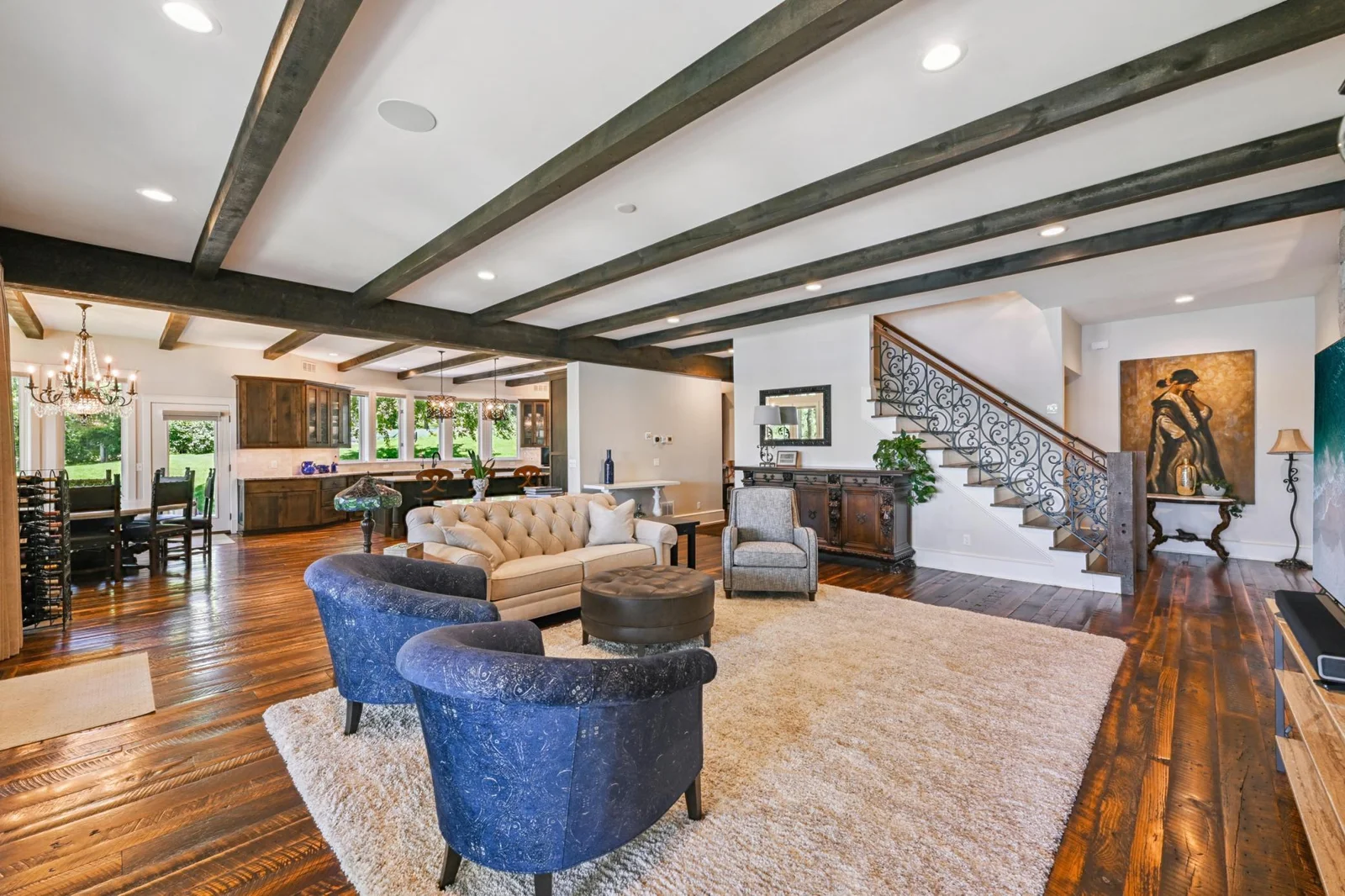 Rich hardwood floors, exposed ceiling beams, and ornate ironwork define this open concept living space seamlessly connecting the great room, dining area, and kitchen for effortless entertaining and everyday comfort.