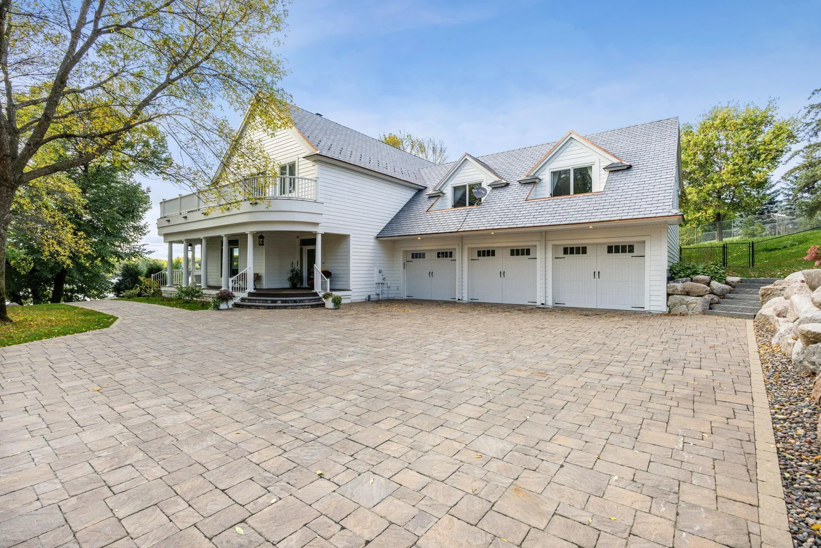 Impressive front elevation featuring a heated paver driveway, charming wraparound porch, and oversized three-stall garage. Classic architectural details and manicured grounds set the tone for this exceptional lakeshore estate.