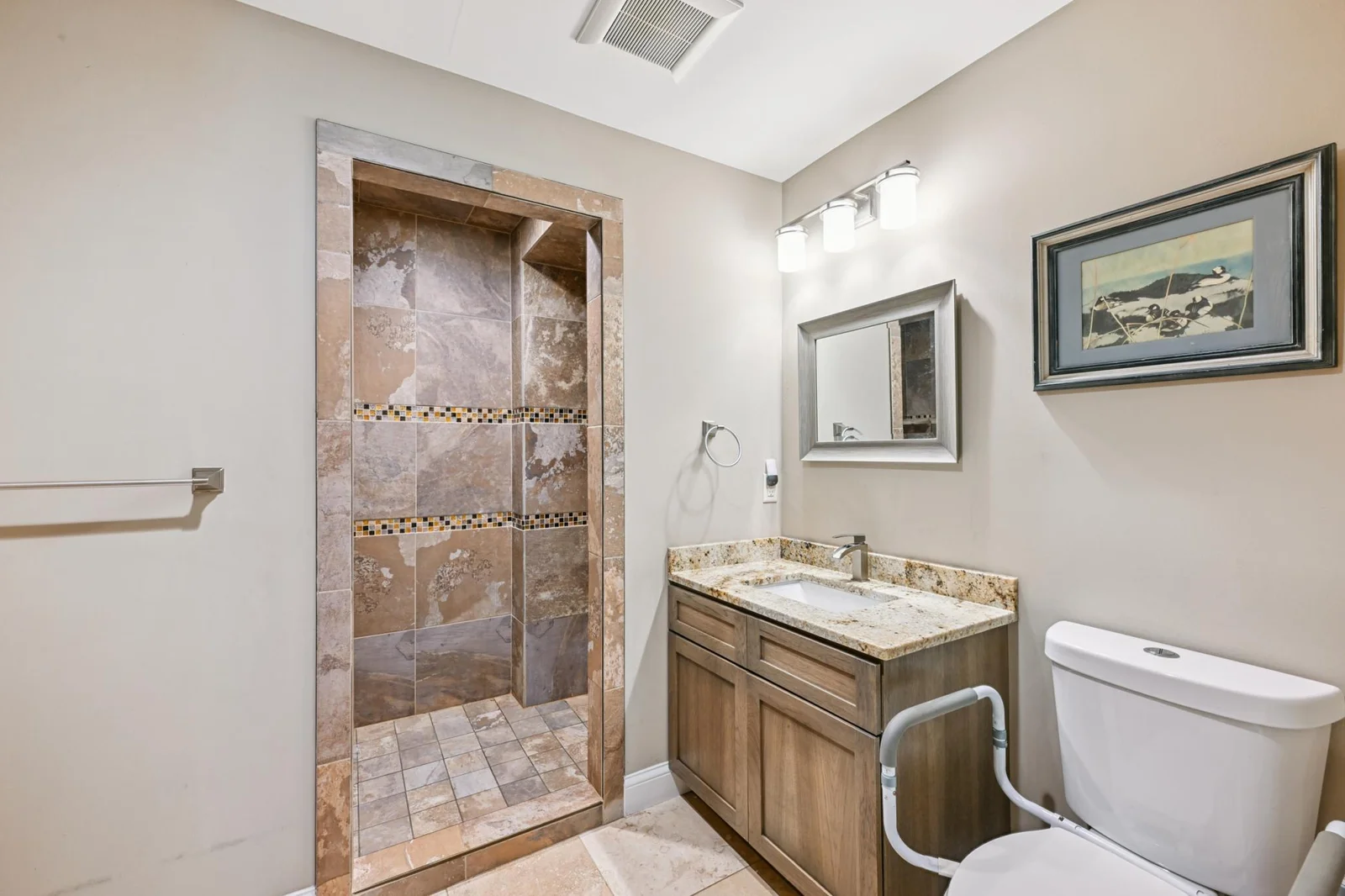 Stylish guest house bathroom featuring a walk-in tile shower with decorative mosaic accents, granite vanity, and modern lighting. A well-appointed space that complements the comfort and quality of this lakeshore retreat.