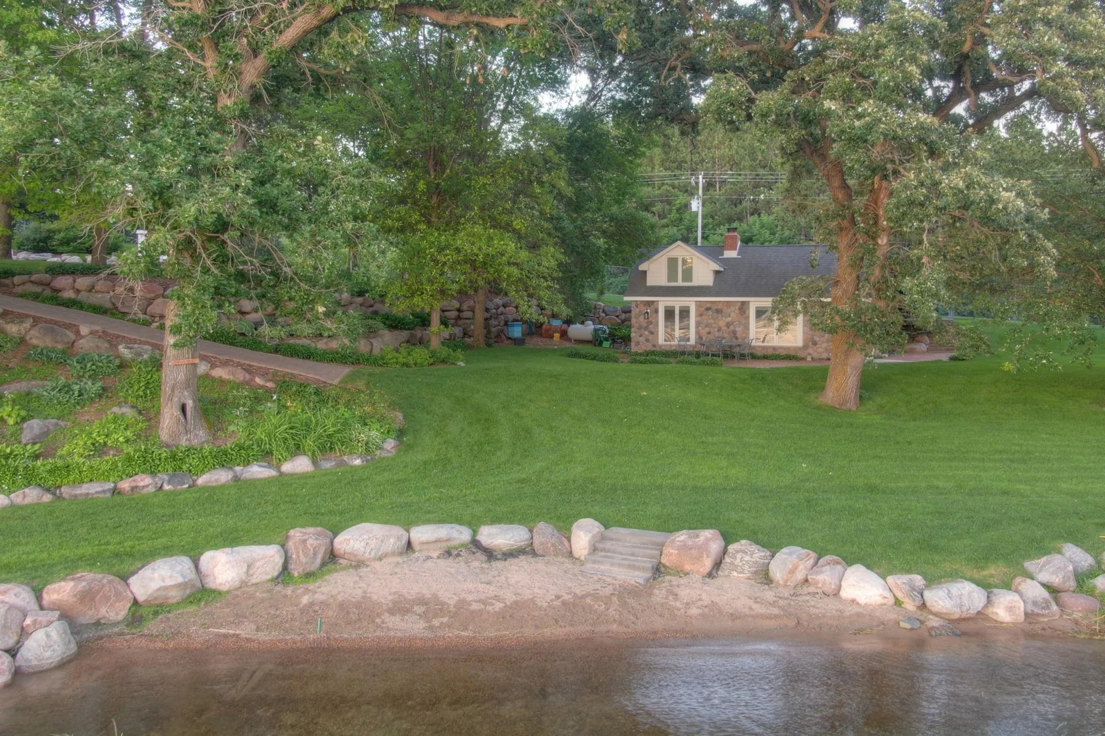 The charming lakeside guest cottage features updated stonework and siding 2020-2021 with the sand beach landscaping added at that time as well.