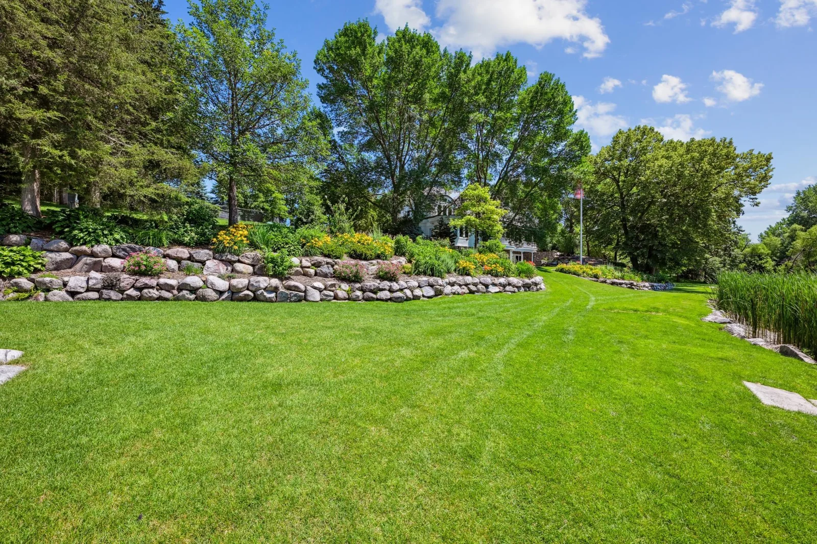 Impeccably landscaped grounds showcase tiered boulder walls adorned with vibrant perennials and mature trees, creating a lush, resort-like setting. The slow sloping lot and landscaping provide both beauty and function at this Lake Sylvia estate.