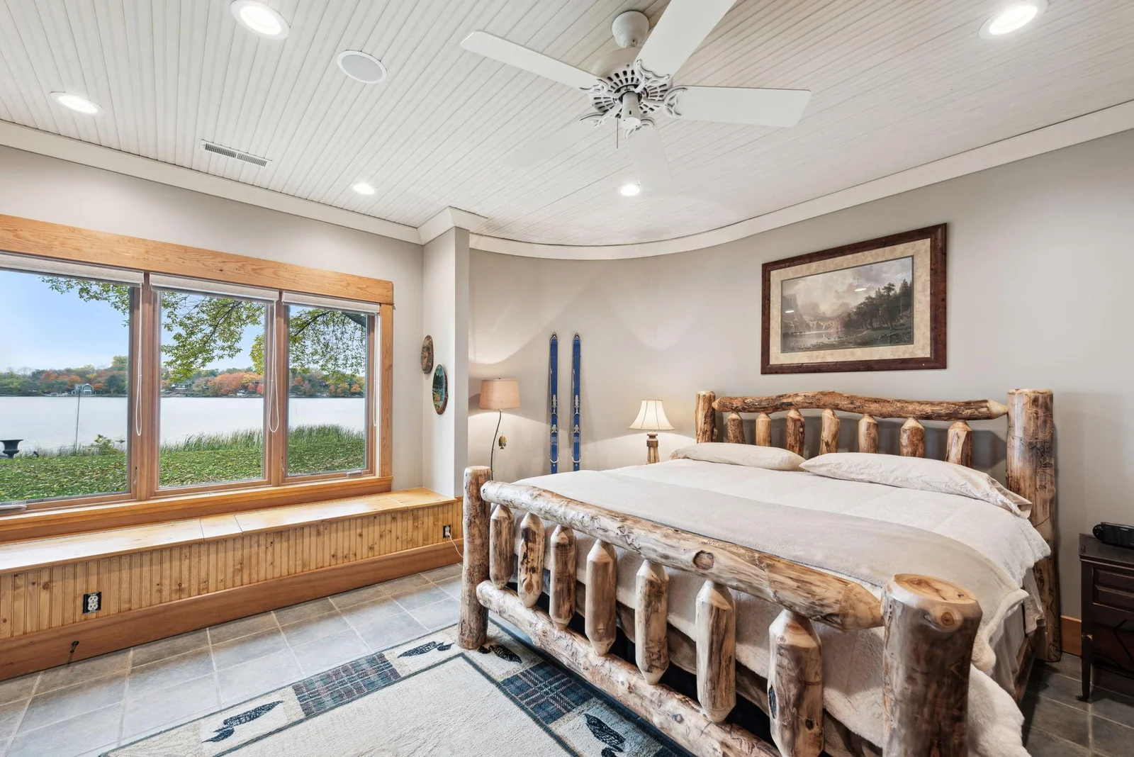Lower-level bedroom with stunning lake views features a built-in bench with storage, tiled floors, and a cozy lodge-style ambiance. Ready for your guests to relax after a day on the water.
