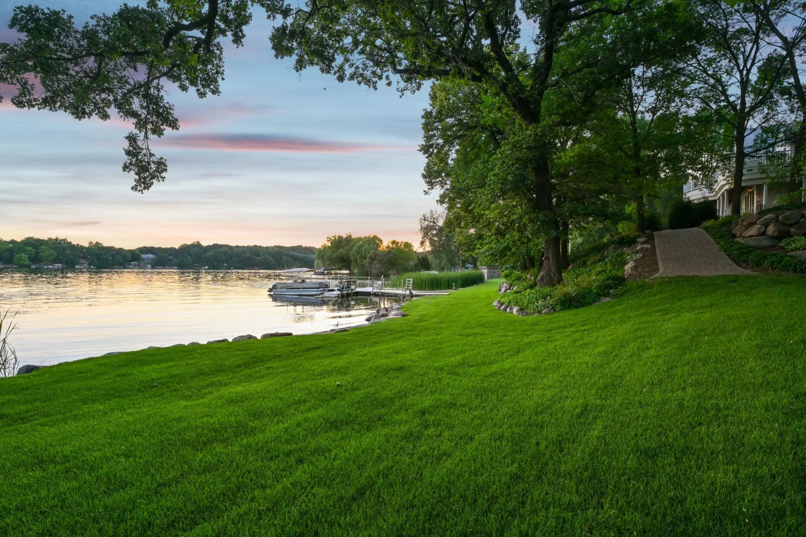 Enjoy a serene, park-like setting with paver pathways, mature trees, boulder-edged gardens, and lush lawn stretching to 385 feet of pristine shoreline on West Lake Sylvia.