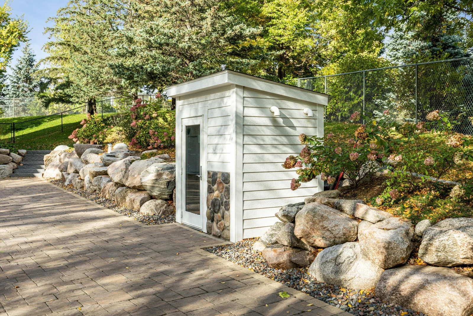 Discreetly tucked into the landscape, this custom utility shed houses the mechanical systems for the heated paver driveway. Thoughtfully designed to blend with the home's exterior, it ensures year-round convenience without compromising aeshetics.