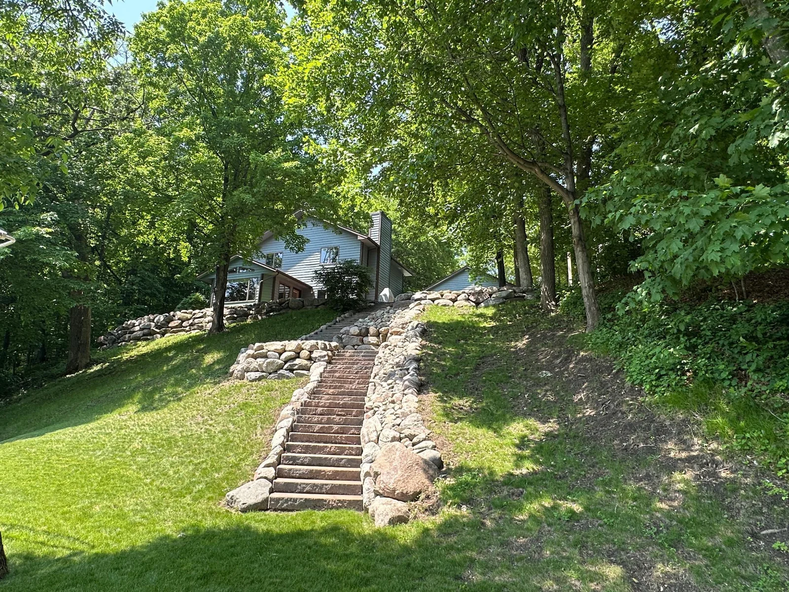 Beautiful, tiered landscaping with boulder walls and stone staircase leading you to the lake.  Many mature trees, and perennials offering many shades of green.